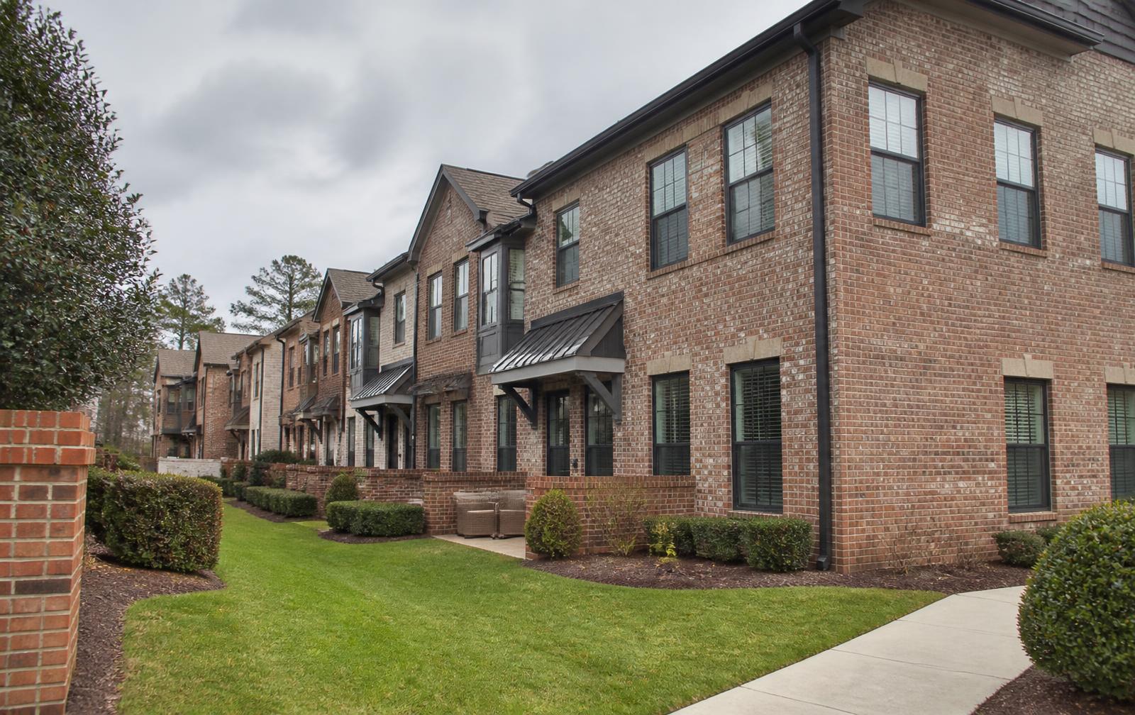 Attached brick townhome-style residences with individual entries, awnings and clipped planting on a landscaped common green